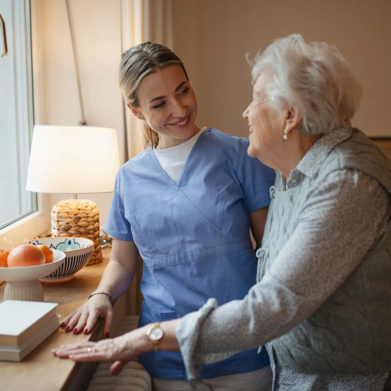 Caregiver smiling with elderly woman by window